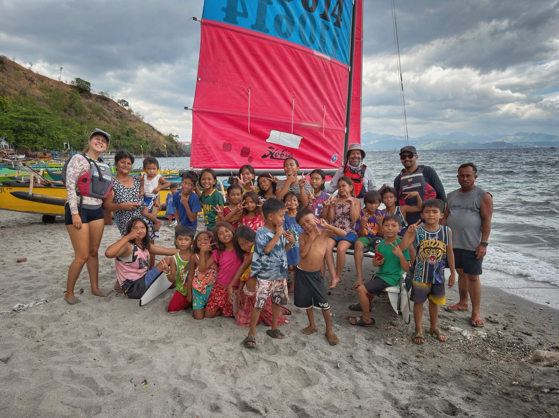 Beach welcome — kids and locals gather around sail #110614 on a coastal stop.